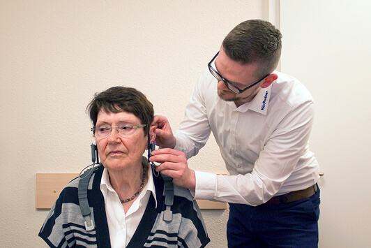 Ein Hörakustiker passt einer älteren Frau ein Hörgerät zur Hörtest-Diagnostik an.