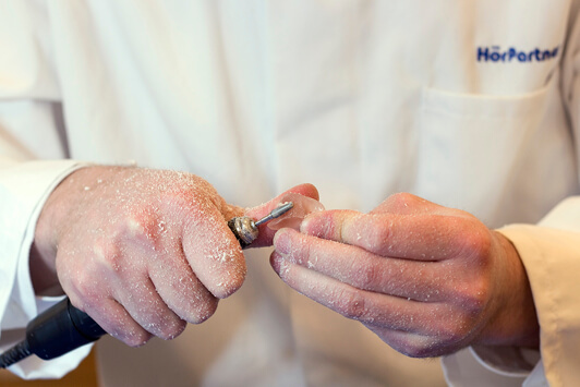 Ein Hörakustiker schleift ein Hörgerät präzise zur individuellen Anpassung per Hand.
